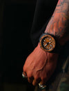 Hand wearing a wooden watch with intricate design on a dark background